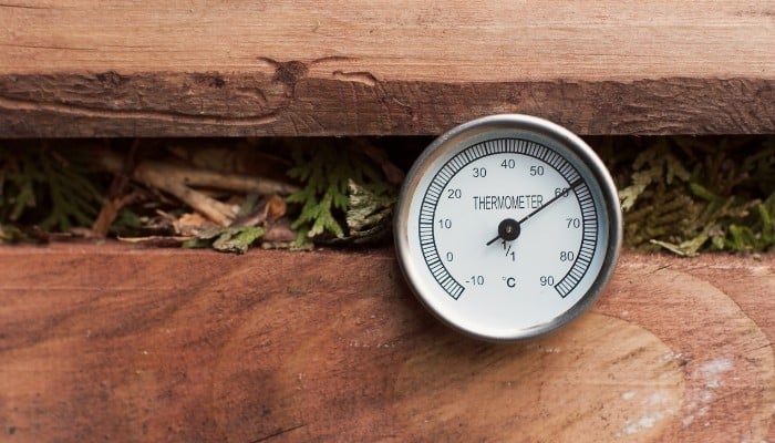 A wooden compost bin with a thermometer stuck into the pile between the slats.