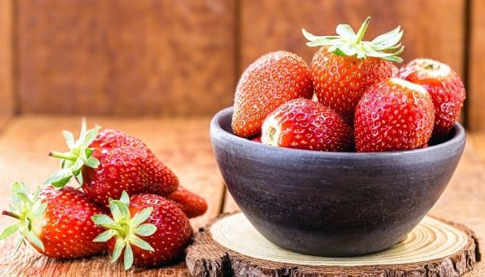 A rustic scene with Albion strawberries in a wood bowl and on a table.