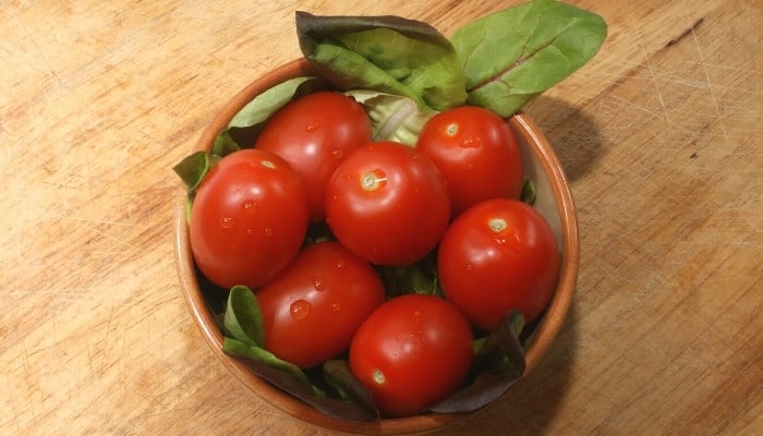 A bowl of organic plum tomatoes and salad leaves on a wood table.