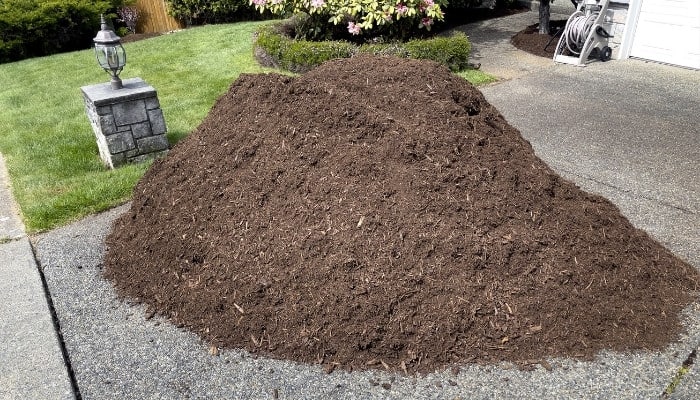 A pile of fresh topsoil in a driveway of a well-manicured yard.