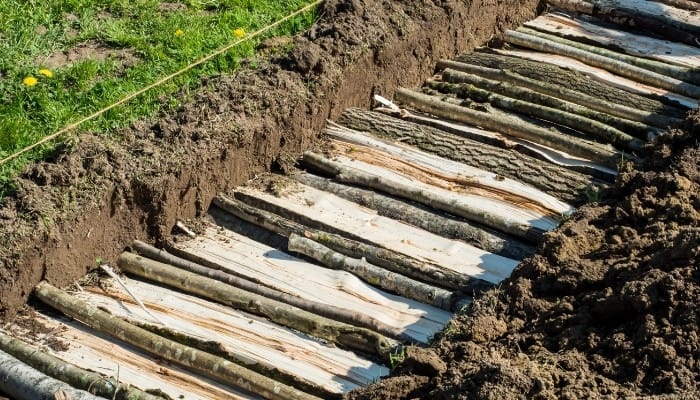 A trench filled with split logs in preparation for a hugelkultur bed.