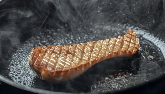 Half of a king oyster mushroom frying in a cast iron pan.