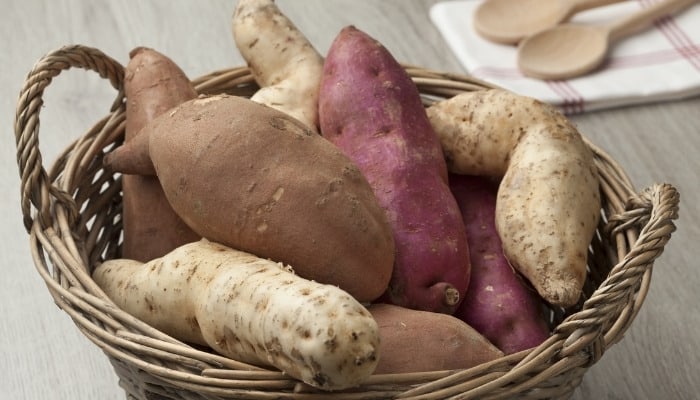 Sweet potatoes, white potatoes, and purple potatoes in a wicker basket.