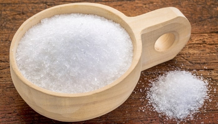 A hand-hewn wooden bowl filled with Epsom salts on a table.