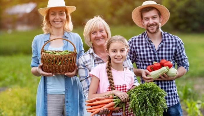 A farming family together outside holding various home-grown produce.