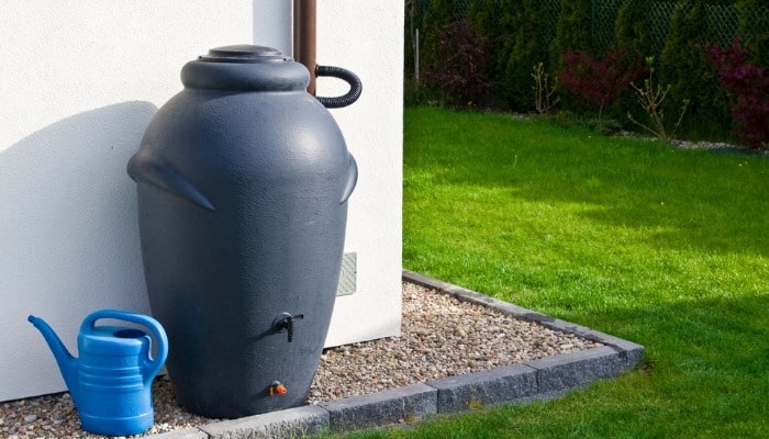A modern, gray rain barrel with a formal garden in the background.