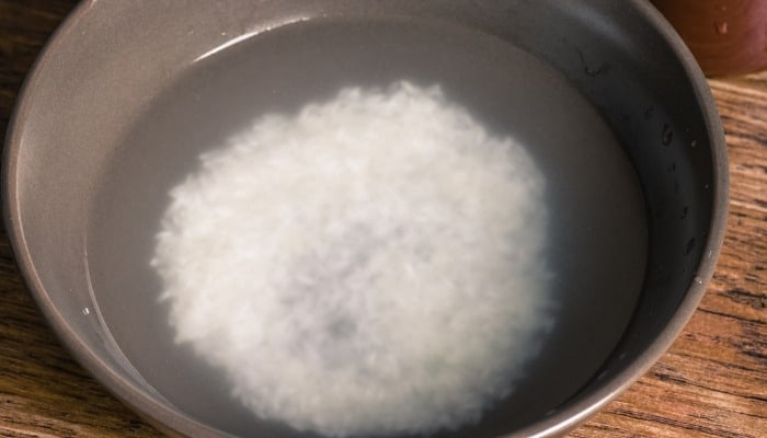 Rice soaking in water in a gray bowl.