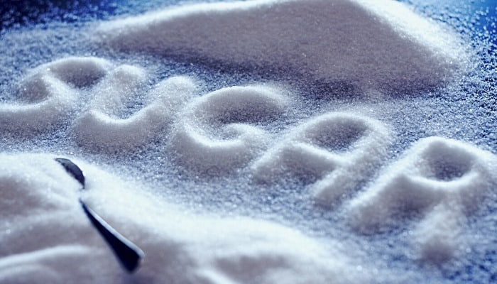 The word sugar spelled out on a table by using actual sugar.
