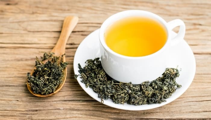 A cup of tea with dried tea leaves on saucer and in wooden spoon.