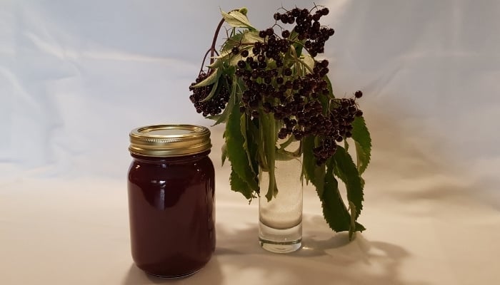 Elderberry syrup in mason jar beside a vase with fresh berries.