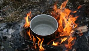 A pot of water coming to a boil over a campfire outside.