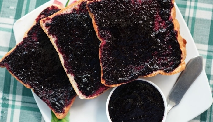 Homemade mulberry jam in a bowl and spread on several pieces of toast.