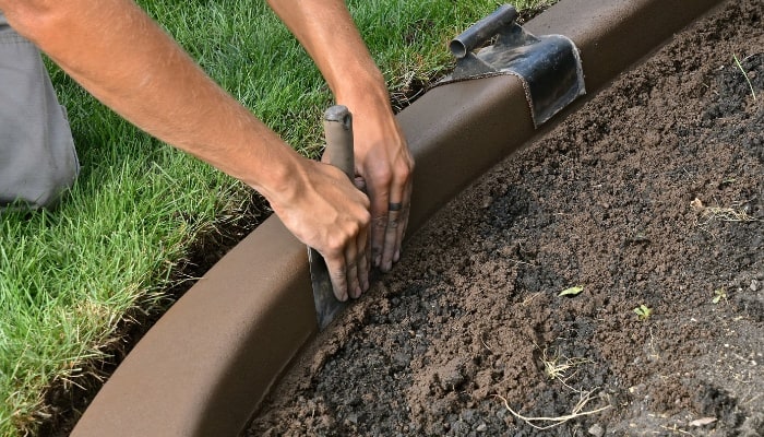 A man smoothing a freshly made concrete garden border.