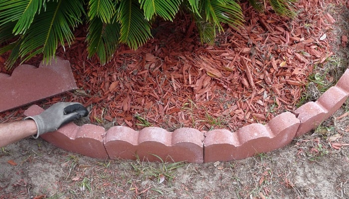 Pre-formed red concrete garden edging being arranged in garden bed.