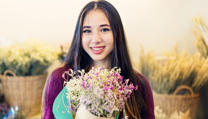 A smiling woman holding a fresh-cut flower bouquet.