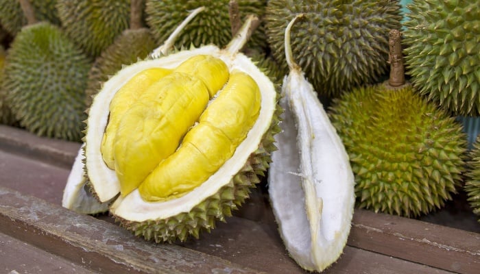 A durian cut open to reveal the flesh and seeds lying in front of whole durians.