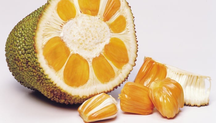 An open jackfruit with seeds lying in front of it.