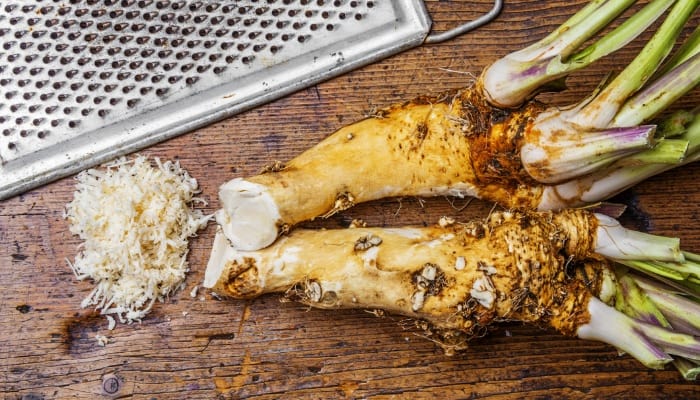 Two horseradish roots on a table beside a grater.